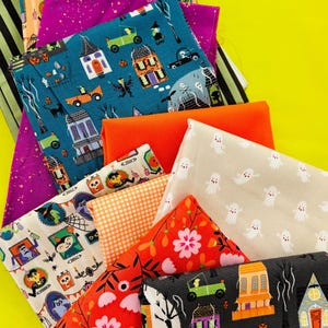 Può includere: Una collezione di quadrati di tessuto piegati con vari motivi, tra cui illustrazioni a tema Halloween di case, fantasmi e personaggi, insieme a stampe a righe arancioni, viola e nere, e disegni floreali in arancione e rosa brillante.