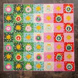 May include: A square patchwork quilt featuring a grid of alternating blocks. One set of blocks displays colorful circular Christmas ornaments with various small motifs, while the other set features bright yellow eight-pointed stars.