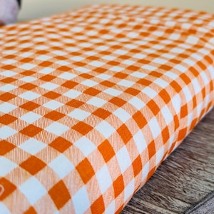 May include: Orange and white checkered fabric with a woven texture.