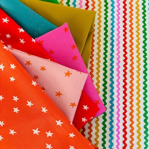 Peut inclure: Une collection de tissus pliés présentant divers motifs et couleurs, notamment orange vif, rouge, rose, bleu sarcelle et jaune moutarde. Certains tissus présentent des motifs d'étoiles blancs ou orange, tandis que d'autres sont unis. Un tissu rayé arc-en-ciel ondulé est visible.