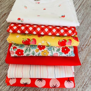 Peut inclure: Une pile de morceaux de tissu pliés dans divers motifs et couleurs. Les tissus comprennent du blanc avec de petites fraises, du vichy rouge, du jaune avec de grosses fraises, des motifs floraux, du rouge uni, du blanc avec des lignes verticales et du rouge avec des illustrations de fraises.
