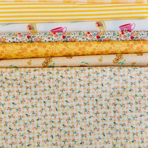 Peut inclure: Une pile de tissus jaunes aux motifs variés. On y trouve des carreaux vichy, des rayures, des motifs floraux et des imprimés de cerises. Les tissus sont roulés et empilés, présentant une variété de textures et de motifs pour la couture et les loisirs créatifs.