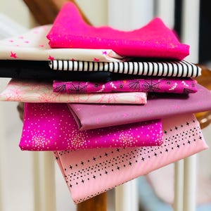 Peut inclure: Une pile de tissus aux motifs variés, dans des tons de rose, noir et blanc. Les motifs comprennent des étoiles, des rayures, des toiles d'araignées et des pois. Idéal pour le patchwork ou les projets de couture.