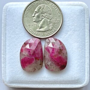 Könnte beinhalten: Zwei facettierte, ovale Edelsteine in leuchtenden Rosa- und Weißtönen werden neben einem US-amerikanischen Vierteldollar gezeigt. Die Edelsteine haben ein poliertes, kristallines Aussehen und weisen innere Muster und Farbvariationen auf. Der Vierteldollar dient als Größenreferenz.