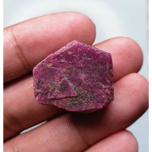 Puede incluir: Una piedra preciosa de rubí rosa intenso con un acabado rugoso y natural. El rubí tiene una forma ligeramente irregular y muestra algunas inclusiones naturales.