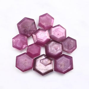 Pode incluir: Um grupo de 10 gemas hexagonais cor-de-rosa. As gemas são facetadas e têm um acabamento brilhante e iridescente.