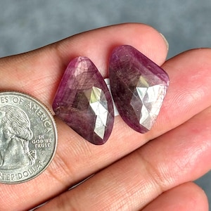 Peut inclure: Deux pierres précieuses magenta à facettes en forme de bouclier avec des inclusions internes visibles et une surface polie, placées à côté d'une pièce de monnaie américaine d'un quart de dollar pour l'échelle, soit 24,26 mm de diamètre.