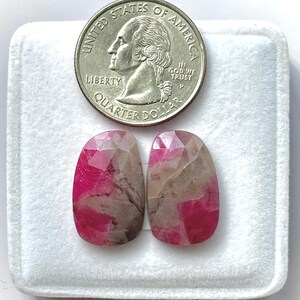 Könnte beinhalten: Zwei ovale Edelsteine ​​mit rosa und beigen Farbtönen werden in einer weißen Box neben einem US-Vierteldollar zur Größenbestimmung präsentiert. Die Edelsteine ​​sind facettiert geschliffen. Der Vierteldollar zeigt das Profil von George Washington. Die Edelsteine ​​sind etwa 2,5 cm lang.