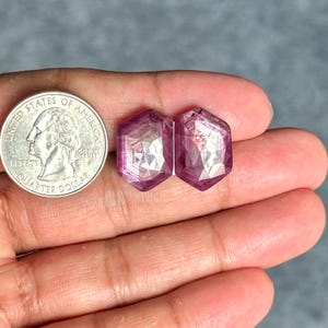 Puede incluir: Dos piedras preciosas facetadas de color rosa con forma hexagonal. Las piedras preciosas son aproximadamente del tamaño de una moneda de 1 euro.