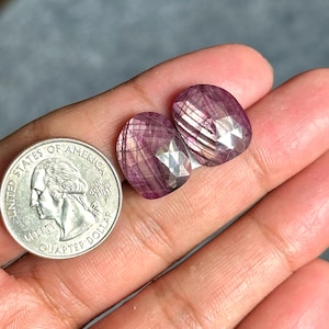 May include: Two faceted, oval-shaped, pink gemstones with internal striations are displayed next to a U.S. quarter. The gemstones have a polished, reflective surface. The quarter shows George Washington's profile.