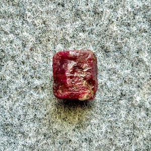 May include: A deep red, square-shaped ruby gemstone. The ruby is faceted and has a glossy finish.