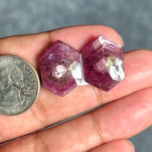 Puede incluir: Dos rubíes magenta facetados de forma hexagonal con inclusiones internas visibles y textura natural. Una moneda de veinticinco centavos de dólar estadounidense está colocada junto a las piedras preciosas para mostrar su tamaño relativo.