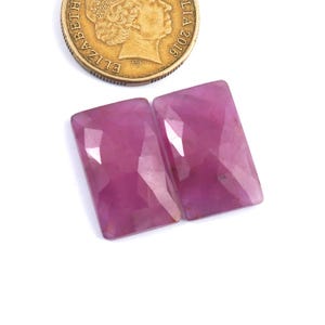 May include: Two rectangular pink gemstones with faceted edges. The gemstones are approximately the size of a UK one pound coin.