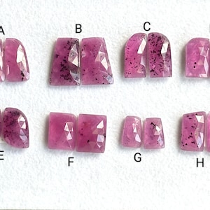 Puede incluir: Ocho pares de cabujones de piedras preciosas rosas y negras, etiquetados de la A a la H. Las piedras preciosas están talladas en varias formas, incluyendo ovalada, rectangular y cuadrada.