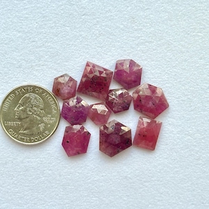 May include: A selection of faceted, reddish-pink gemstones in various shapes, including hexagons and rectangles, are shown beside a U.S. quarter. The gemstones are translucent and are on a white surface.