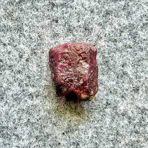 May include: A close-up of a dark red ruby gemstone with a rough, natural texture.