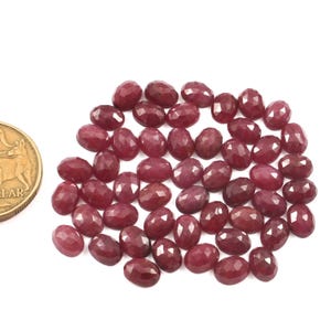 May include: A pile of 40 faceted ruby gemstones, each with a deep red color and oval shape. The gemstones are approximately 10mm in length and 7mm in width.