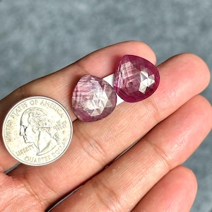 Op de afbeelding: Twee gefacetteerde, druppelvormige, roze edelstenen. De edelstenen worden naast een Amerikaanse kwartdollar getoond ter vergelijking van de grootte. De edelstenen hebben een doorschijnende kwaliteit met zichtbare interne structuren.