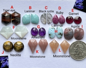 Op de afbeelding: Assortiment van gepolijste edelstenen, waaronder tijgeroog, larimar, zwarte rutiel, robijn, granaat, maansteen, amethist, agaat en neolite. Elke steen is gelabeld met zijn naam.