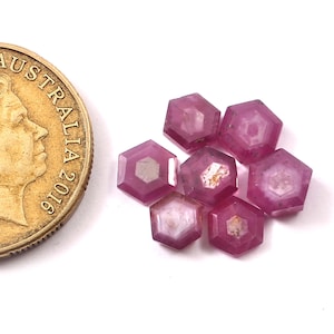 Op de afbeelding: Zes roze zeshoekige edelstenen, elk met een gefacetteerd oppervlak, zijn in een cluster gerangschikt. De edelstenen zijn ongeveer zo groot als een Nederlandse euro.