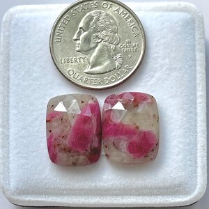 Könnte beinhalten: Zwei facettierte, kissenförmige Edelsteine mit rosa und weißer Färbung. Eine US-Vierteldollarmünze dient zum Größenvergleich. Die Edelsteine liegen in einem weißen Tablett.