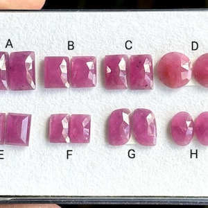 Puede incluir: Ocho pares de cabujones de piedras preciosas rosas expuestos en una tarjeta blanca con letras de la A a la H que etiquetan cada par.