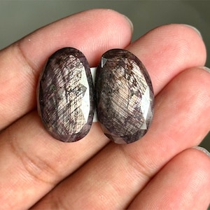 Pode incluir: Duas pedras preciosas ovais de cor cinza escuro com um acabamento brilhante e iridescente.