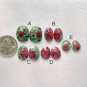 Puede incluir: Una colección de piedras preciosas facetadas, incluyendo formas ovaladas y de lágrima. Las piedras preciosas presentan una mezcla de colores rojo, verde y transparente. Se incluye una moneda de 25 centavos de dólar estadounidense como referencia de tamaño.