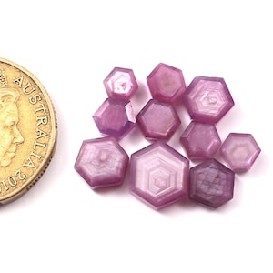 Op de afbeelding: Een groep van tien gefacetteerde roze saffier edelstenen in een zeshoekige vorm. De edelstenen zijn ongeveer zo groot als een Nederlandse 10-cent munt.
