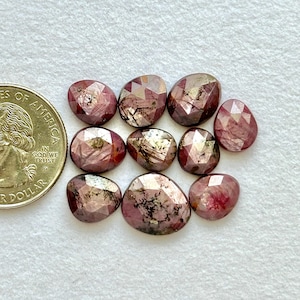 Puede incluir: Colección de nueve gemas facetadas de forma ovalada en tonos rosa y burdeos. Las gemas están dispuestas sobre una superficie blanca. Las gemas tienen un aspecto pulido y reflectante. Las gemas miden aproximadamente 1-2 cm.