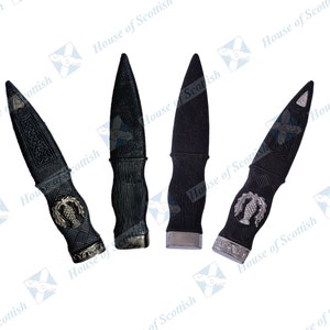 May include: Four black metal sgian dubhs with silver accents. Each sgian dubh has a different design on the handle, including a thistle, a knotwork pattern, and a bird.