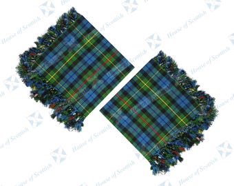 May include: Two square fabric pieces featuring a blue, green, and black tartan plaid pattern with thin yellow and red accent lines. Each piece is finished with a decorative fringe along the edges, incorporating blue, green, and black threads.