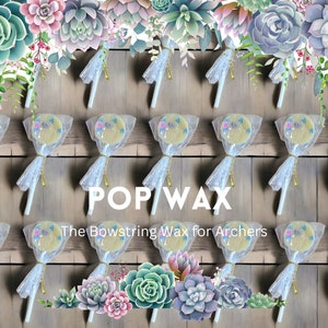 May include: A collection of 18 white and blue bowstring wax lollipops wrapped in clear cellophane and tied with gold ribbon. The lollipops are arranged in rows on a wooden surface. The text "POP/WAX The Bowstring Wax for Archers" is printed on the surface. Succulents are arranged at the top and bottom of the image.