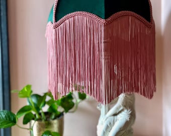 May include: A green velvet lampshade with a pink fringe trim. The lampshade is on a white statue base.