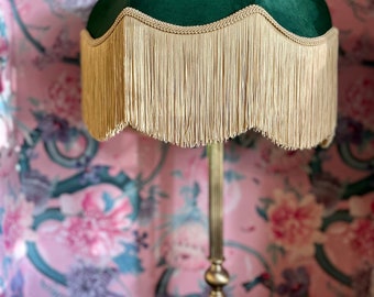May include: A green velvet lampshade with a gold fringe trim. The lampshade is on a gold metal lamp stand.