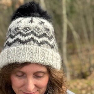 May include: A gray and black knit hat with a black pom pom. The hat has a geometric pattern.