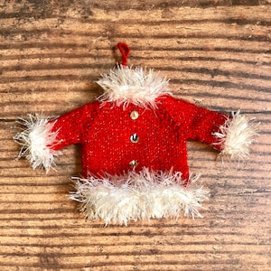 May include: A red knitted Santa Claus sweater ornament with white faux fur trim. The ornament has a loop at the top for hanging.