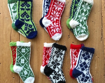 Könnte beinhalten: Sechs Paar gestrickte Weihnachtsstrümpfe in Rot, Grün, Weiß und Blau mit Schneeflocken- und geometrischen Mustern.