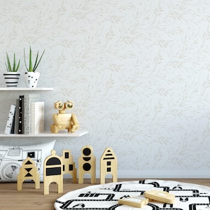 May include: A white wall with a light brown floral pattern. A wooden shelf with two potted plants, books, and a wooden robot toy. A white pillow with a camera graphic. A black and white play mat with a road design. Wooden toy blocks with black geometric shapes.