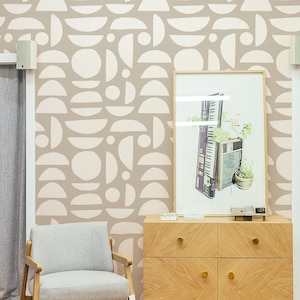 Peut inclure: Un mur brun clair avec un motif géométrique de demi-cercles et de cercles blancs. Une commode en bois avec deux tiroirs se trouve devant le mur. Une estampe encadrée d'un clavier et de plantes est posée sur la commode. Un fauteuil gris clair se trouve devant la commode.
