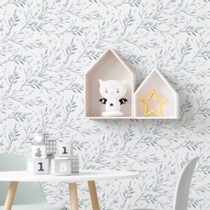 May include: A white wall with a light blue watercolor floral pattern. There are two white shelves with a white bat nightlight and a yellow star on them. A white table with a light green chair is in the foreground. There are wooden blocks with numbers on them on the table.