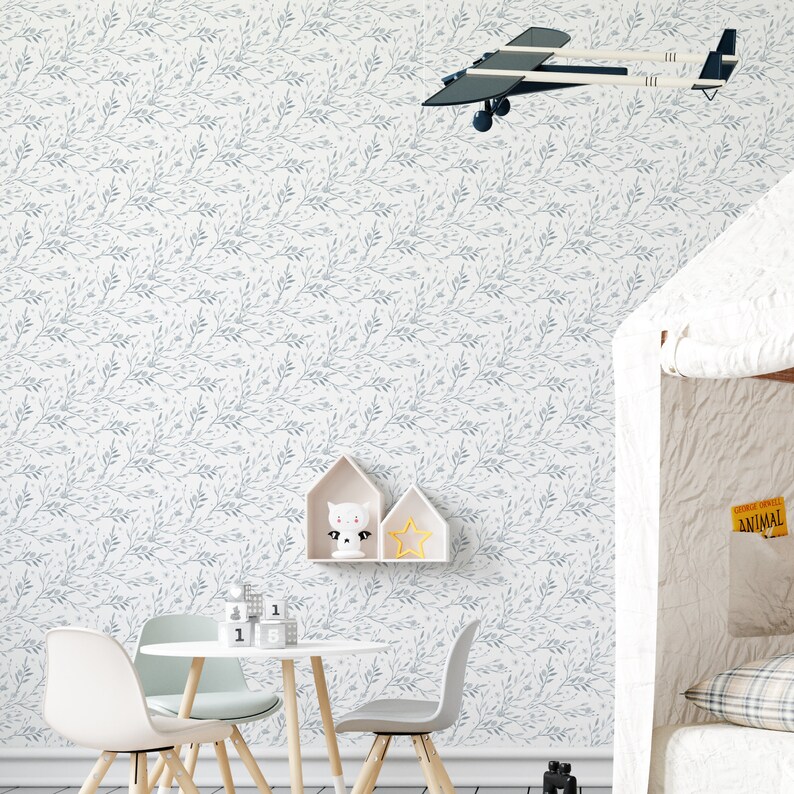 May include: A white wallpaper with a light blue floral pattern. The wallpaper features a repeating pattern of small branches with leaves. The wallpaper is shown in a room with a table and chairs, a toy airplane hanging from the ceiling, and a small shelf with a toy cat and a star.