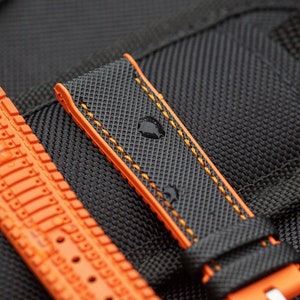 Puede incluir: Una correa de reloj negra con costuras naranjas. La correa tiene una superficie texturizada y est&aacute; hecha de un material duradero.