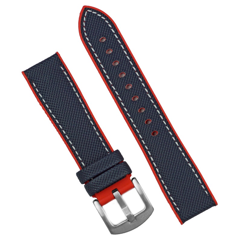 Puede incluir: Una correa de reloj azul oscuro con costuras rojas y una costura de contraste blanca. La correa tiene una hebilla de acero inoxidable.