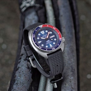 May include: A stainless steel Seiko PADI automatic diver's watch with a blue dial, red and blue bezel, and a black rubber strap. The watch features a day and date display and is designed for diving.