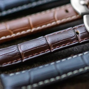 May include: Close-up of several leather watch straps in varying shades of brown and blue. The straps have a textured, crocodile-like pattern and are stitched with white thread. The image highlights the detail and craftsmanship of the watch bands.