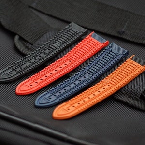 Puede incluir: Cuatro correas de reloj en diferentes colores: negro, rojo, azul y naranja. Cada correa tiene un patr&oacute;n texturizado y est&aacute; hecha de goma.