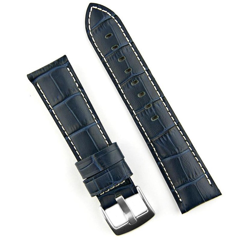 May include: A navy blue watch strap with a crocodile pattern and white stitching. The strap has a silver-colored buckle and is made of a textured material. The watch band is a replacement part.