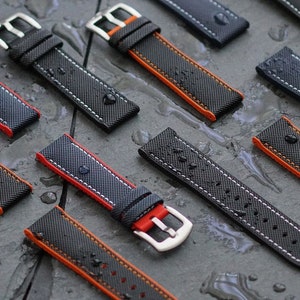 Puede incluir: Una colecci&oacute;n de correas de reloj negras con costuras naranjas. Las correas tienen una superficie texturizada y una hebilla plateada.