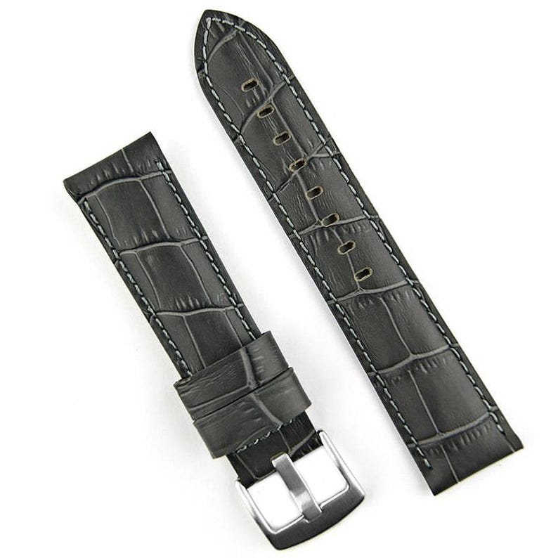 May include: A pair of dark gray watch straps with a crocodile skin texture. The straps are stitched with white thread and have a silver-colored buckle. The watch straps are approximately 8 inches long.